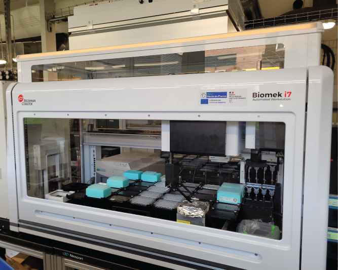 Photographie d'une station de pipetage automatique Biomek i7 à paroie vitrée à travers laquelles le robot de pipetage est visible. 